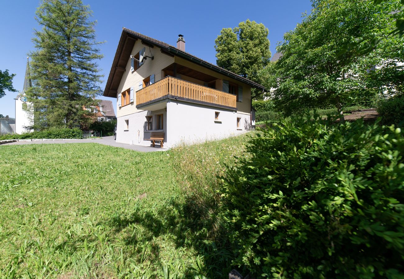 Maison de vacances avec balcon en bois, grand jardin et cadre verdoyant par temps ensoleillé.