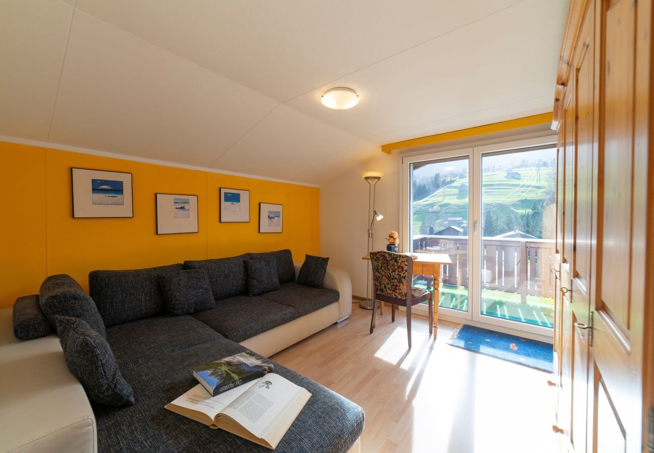 Salon lumineux avec canapé d’angle, accès au balcon et vue sur les montagnes du Toggenburg